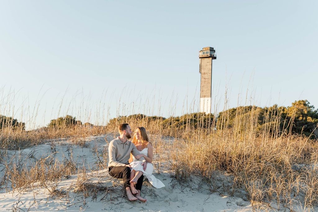 Caroline and Jamie sitting on the beach with the Sullivan’s Island lighthouse in the background
