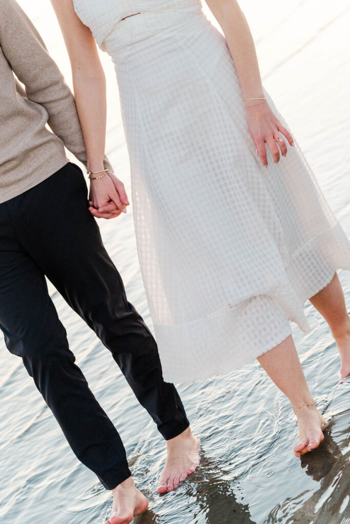 Couple walking through shallow ocean water during their Sullivan’s Island engagement photos
